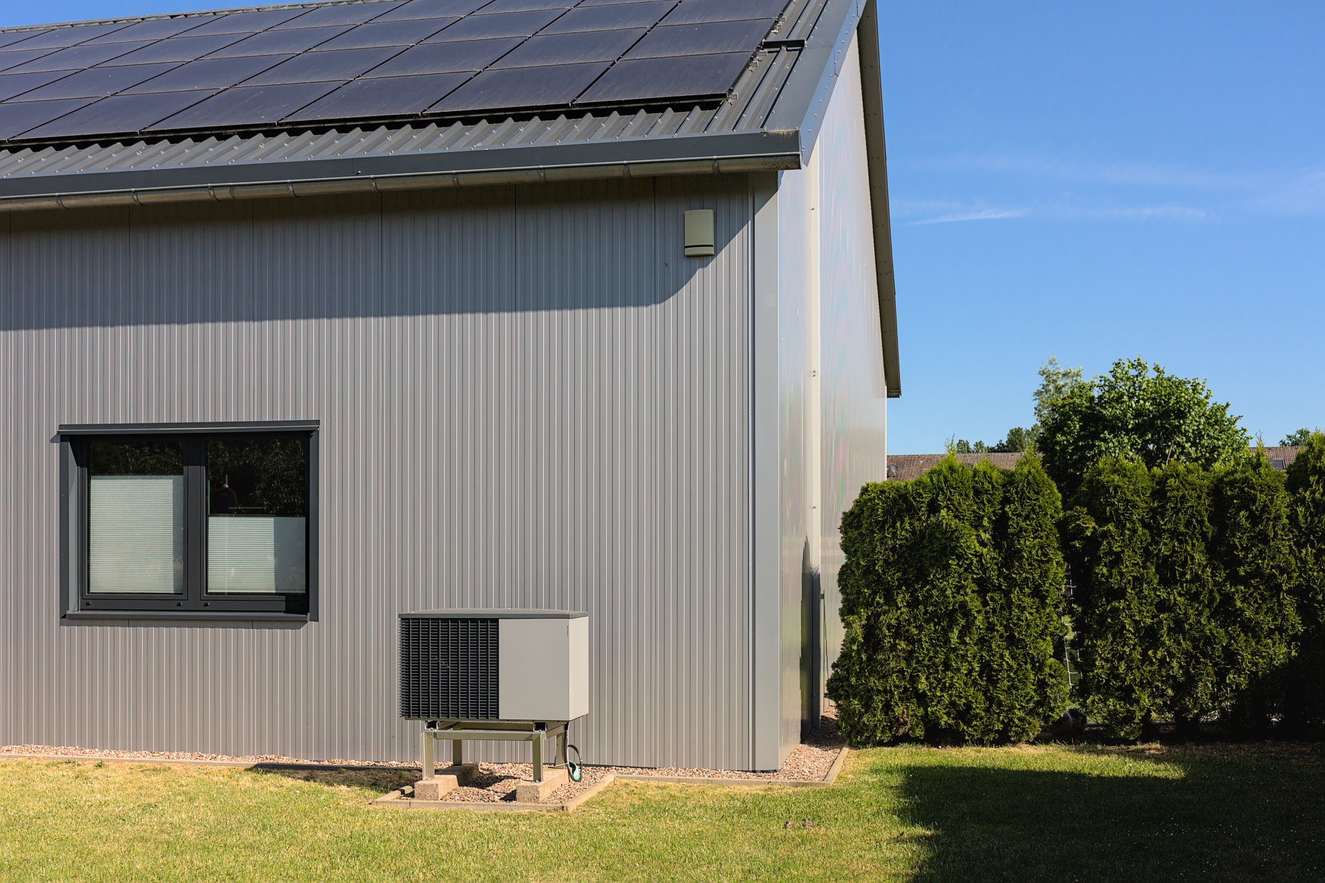 Foto, Seitenansicht eines modernes Einfamilienhaus mit einer Solaranlage auf dem Dach und eine davor aufgestellten Wärmepumpe.