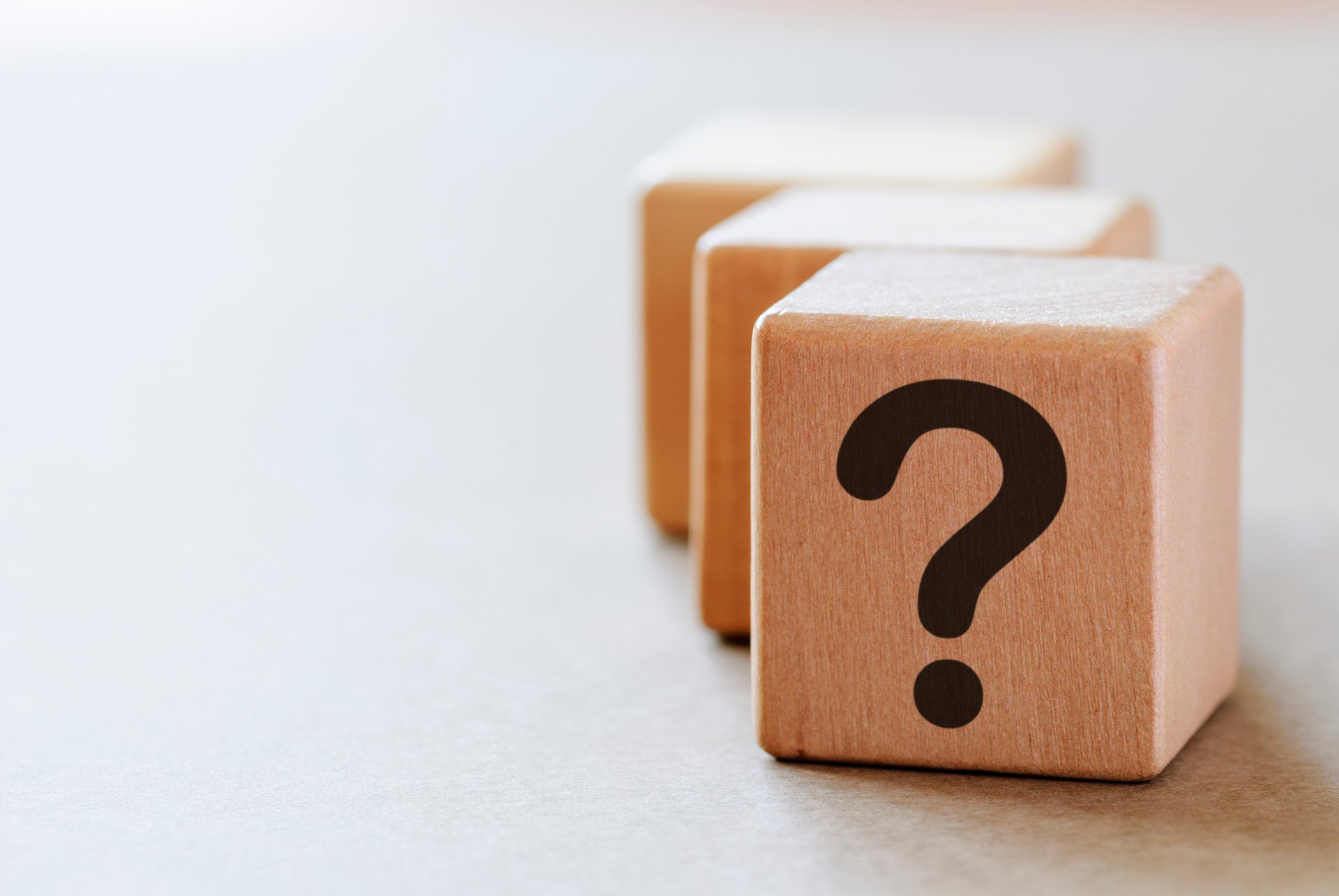 Foto, drei Holzwürfer in Reihe hintereinander auf heller Oberfläche, auf dem ersten Würfel ist ein Fragezeichen abgebildet.