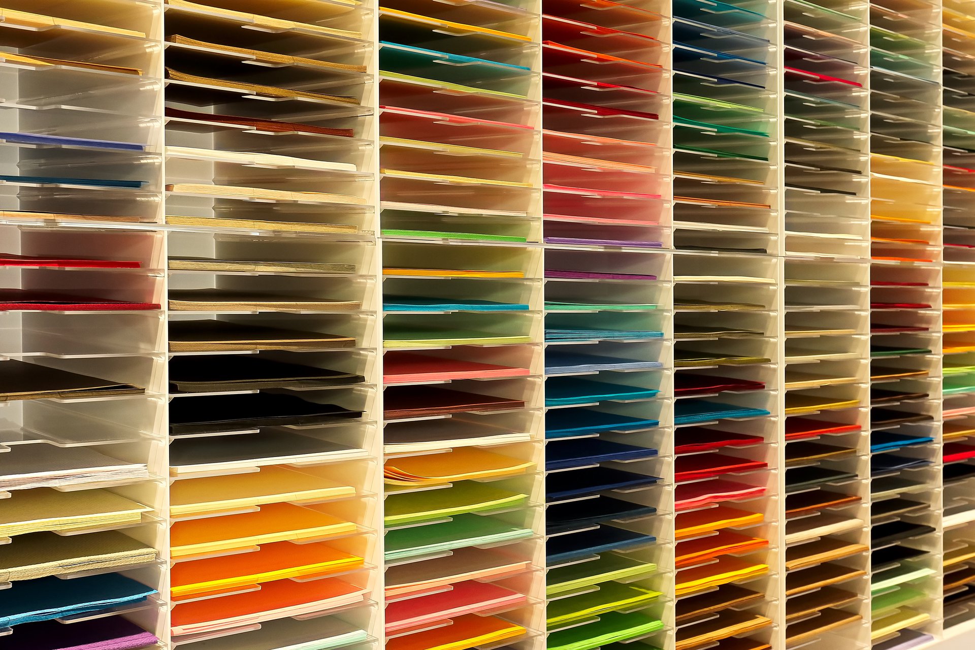 Foto, ein Regal mir vielen schmalen Fächern, in denen verschiedenfarbiges Papier liegt.