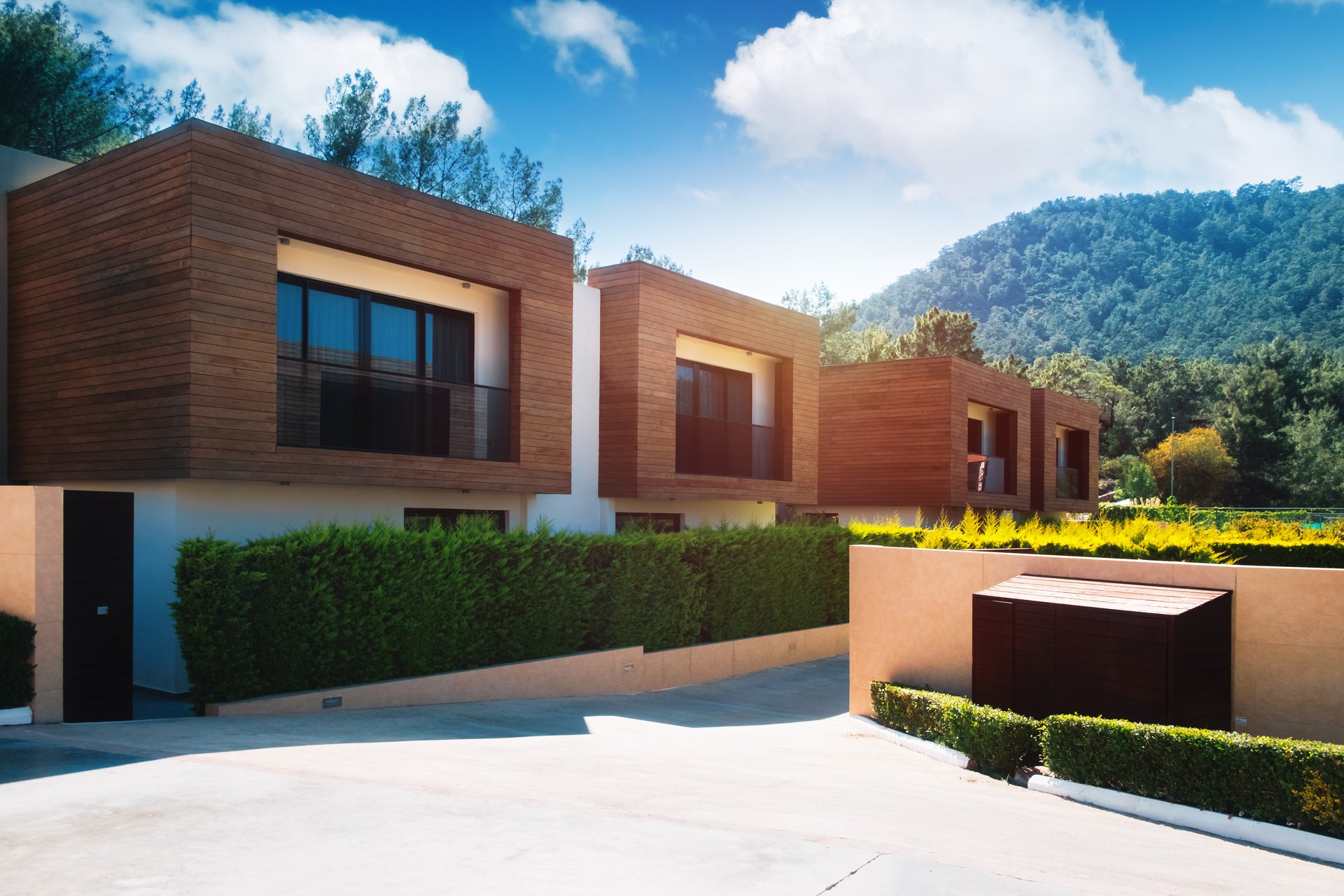 Foto, Blick auf mehrere, neu gebaute und modern anmutende Wohnhäuser. Im Hintergrund grüne, bewaldete Hügel.