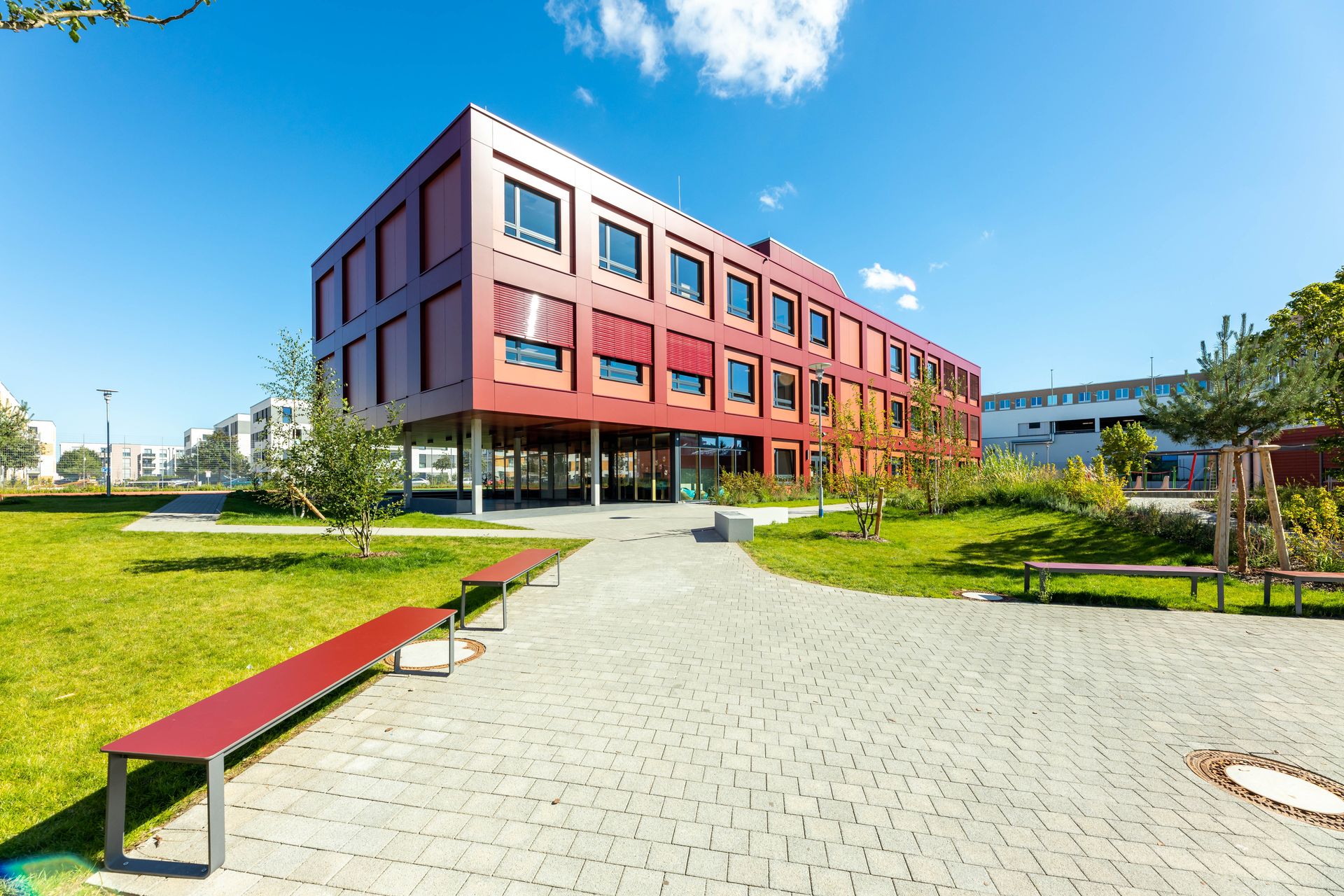 Foto, Außenansicht eines roten Gebäudes mit zwei Stockwerken. Im Vordergrund befinden sich ein Weg und Grünflächen.